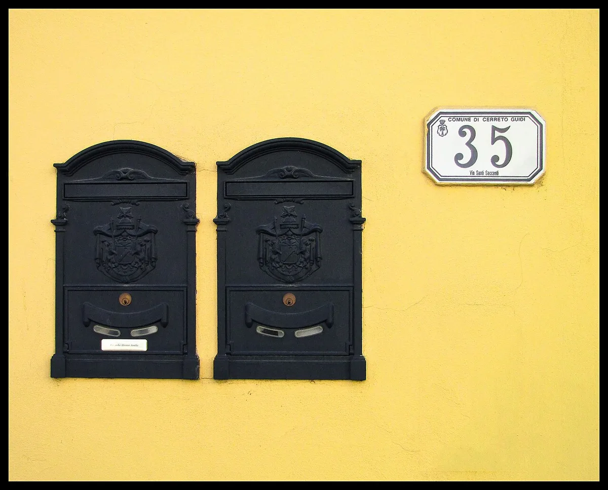 Deux boîtes aux lettres murales anthracite à blason en relief sur une façade crépie jaune, à côté d'une plaque émaillée portant le numéro 35.